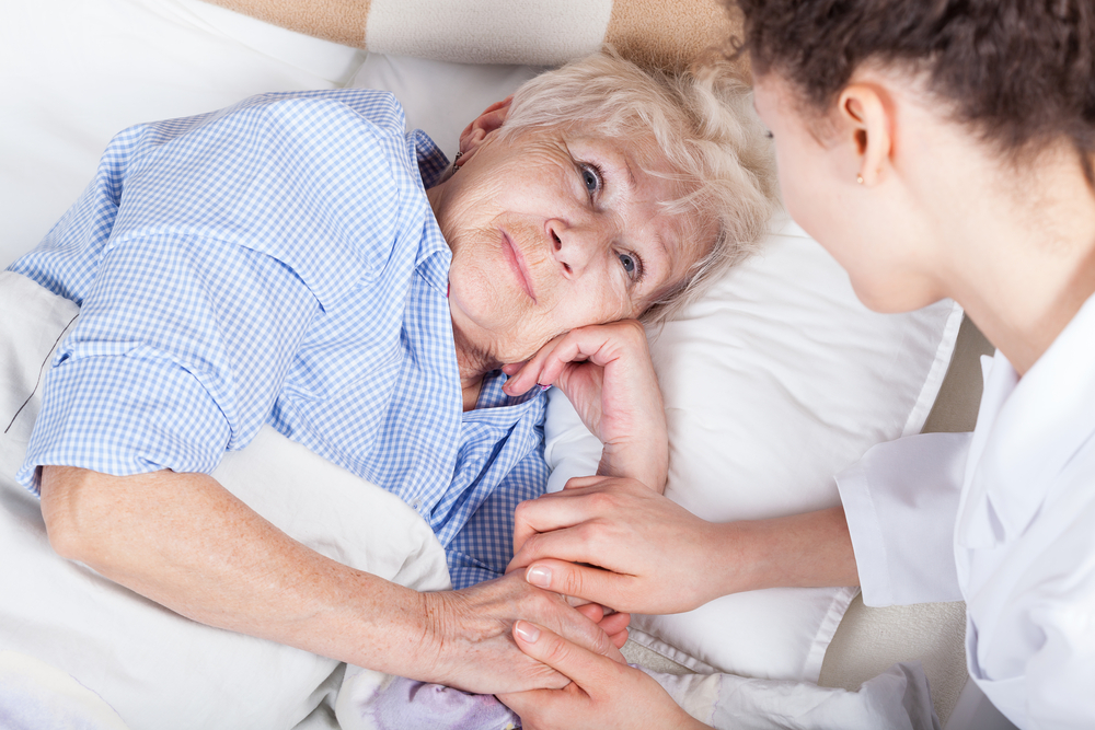 Senior lady in bed with caregiver on the side